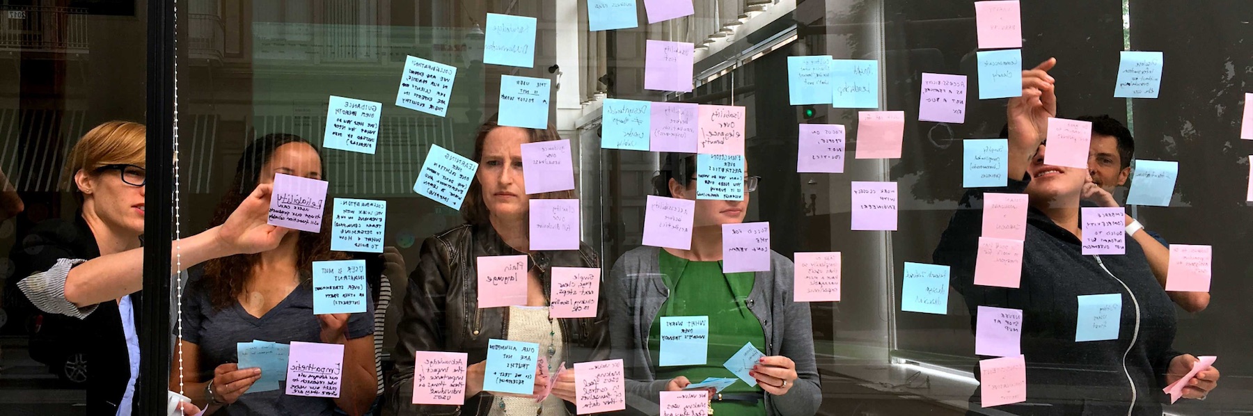 Ad Hoc staff pointing to a wall of Post-It notes on glass during an affinity mapping exercise.