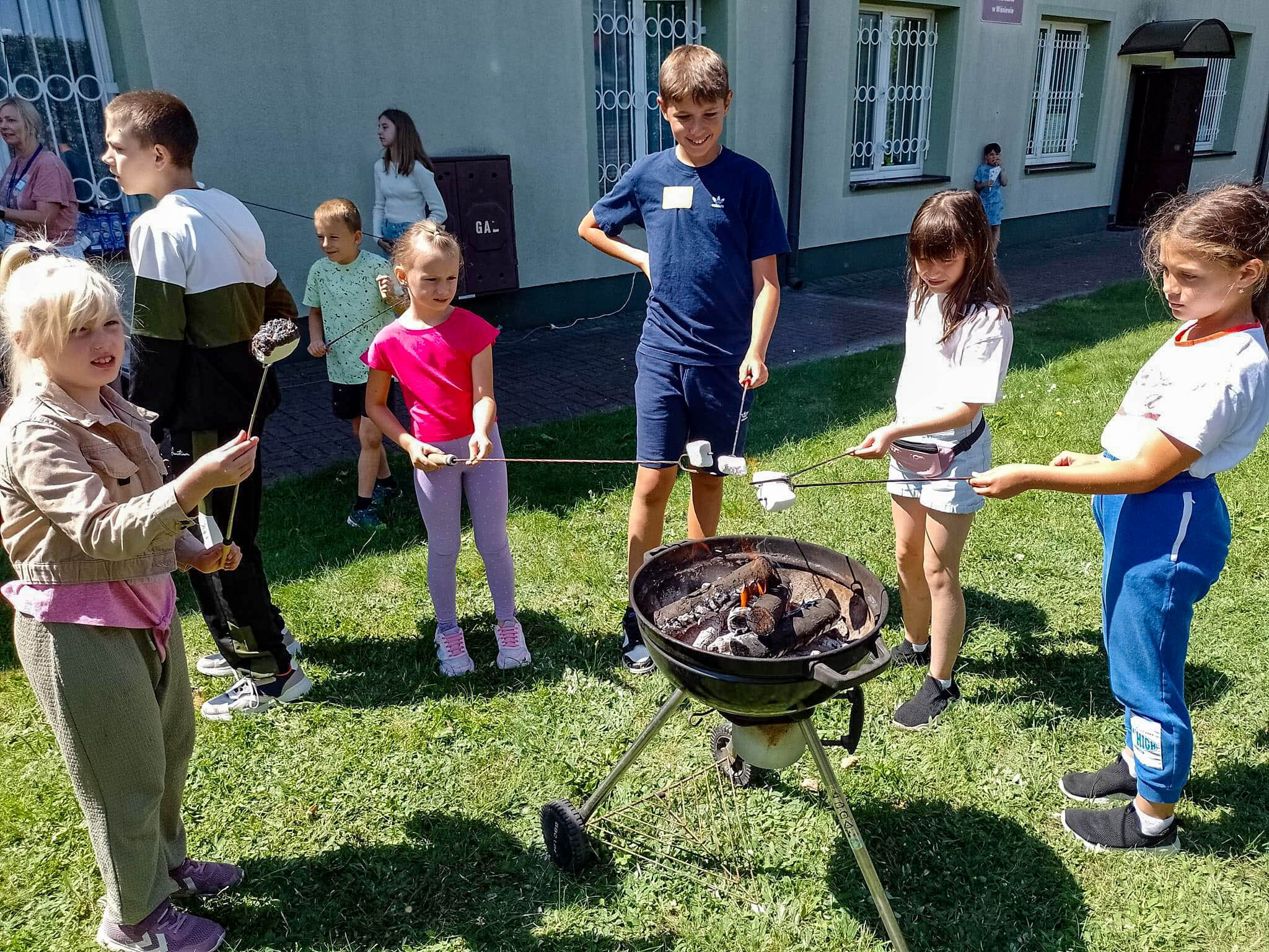 Summer camp attendees outside, roasting marshmallows over a grill.