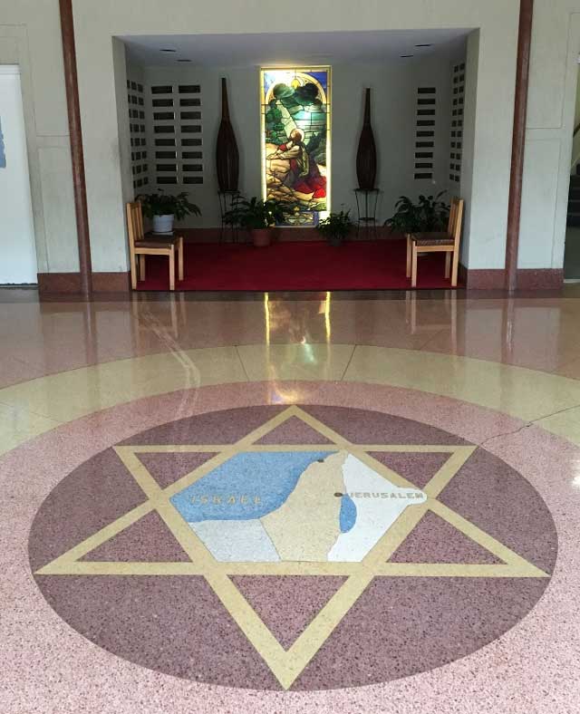 Detail of the floor of the Nineteenth Street Baptist Church. A gold Star of David contains a map of Israel with Jerusalem labeled. In the background is a stained glass window with an image of Jesus.